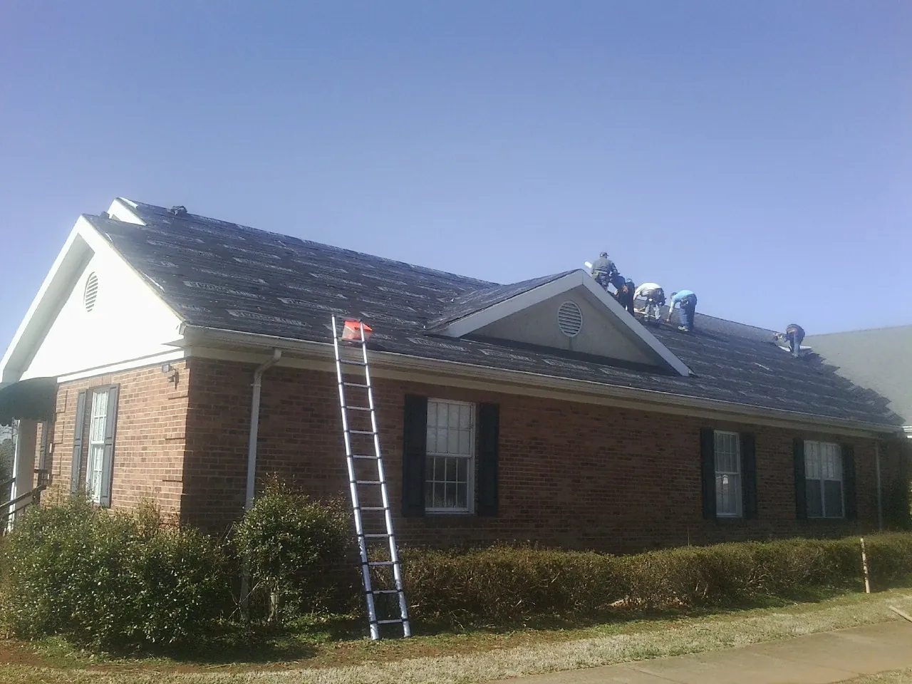 Crew tearing shingles off a brick ranch roof with a ladder set — Metal Roof Repair work by our crew in Du Bois