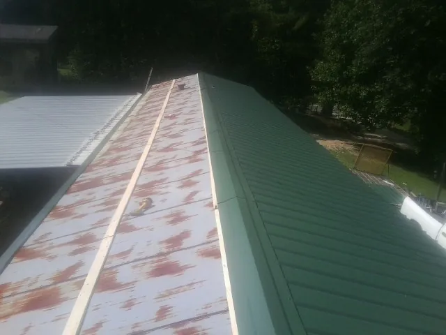 Old rusted panels beside newly installed green metal roofing — Wind Damage Roof Repair by Roofing Brothers in Du Bois