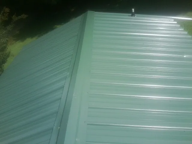 New green metal panels meeting at the ridge of a roof — Flat Roof Repair work by our crew in Du Bois