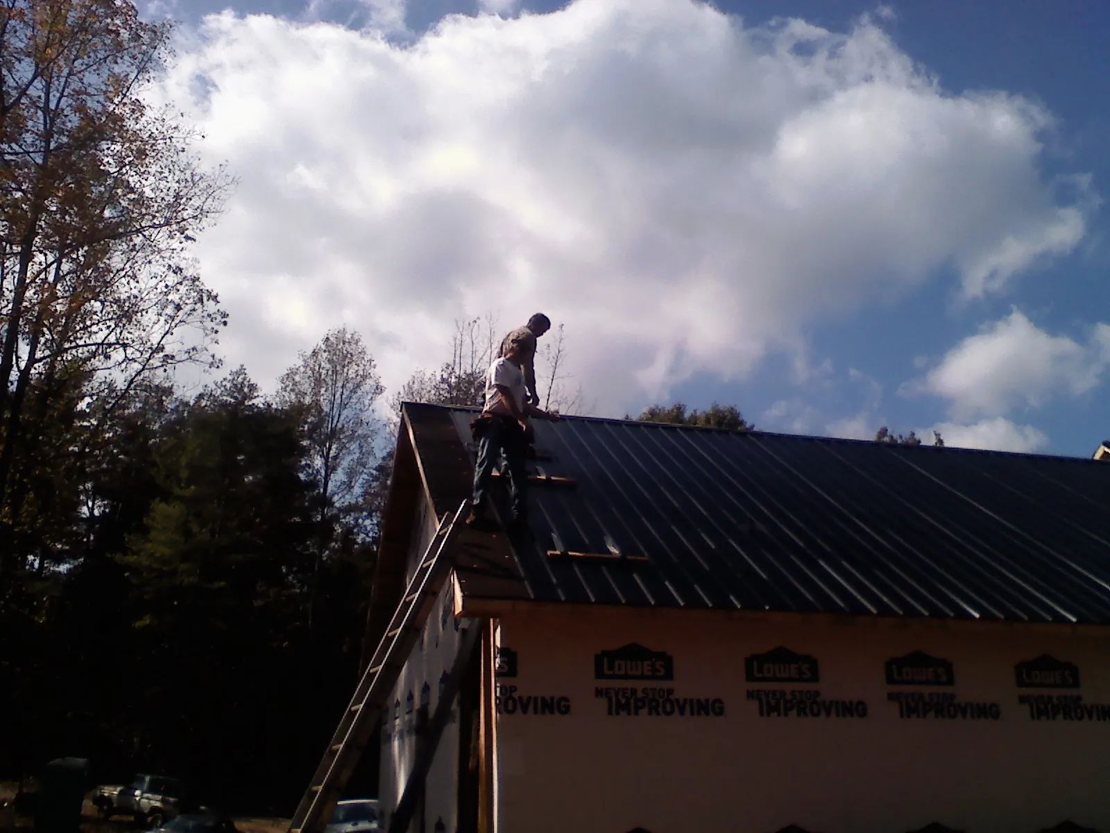 Roofer fastening dark metal panels high against a cloudy sky, from a Roof Inspection job in Du Bois