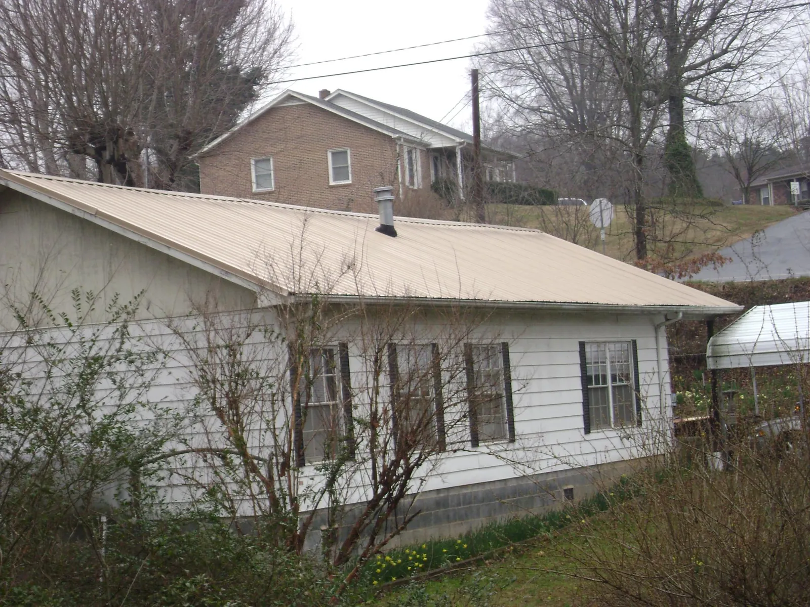 Tan metal roof on a white sided house set into a hillside — Commercial Roofing by Roofing Brothers in Du Bois