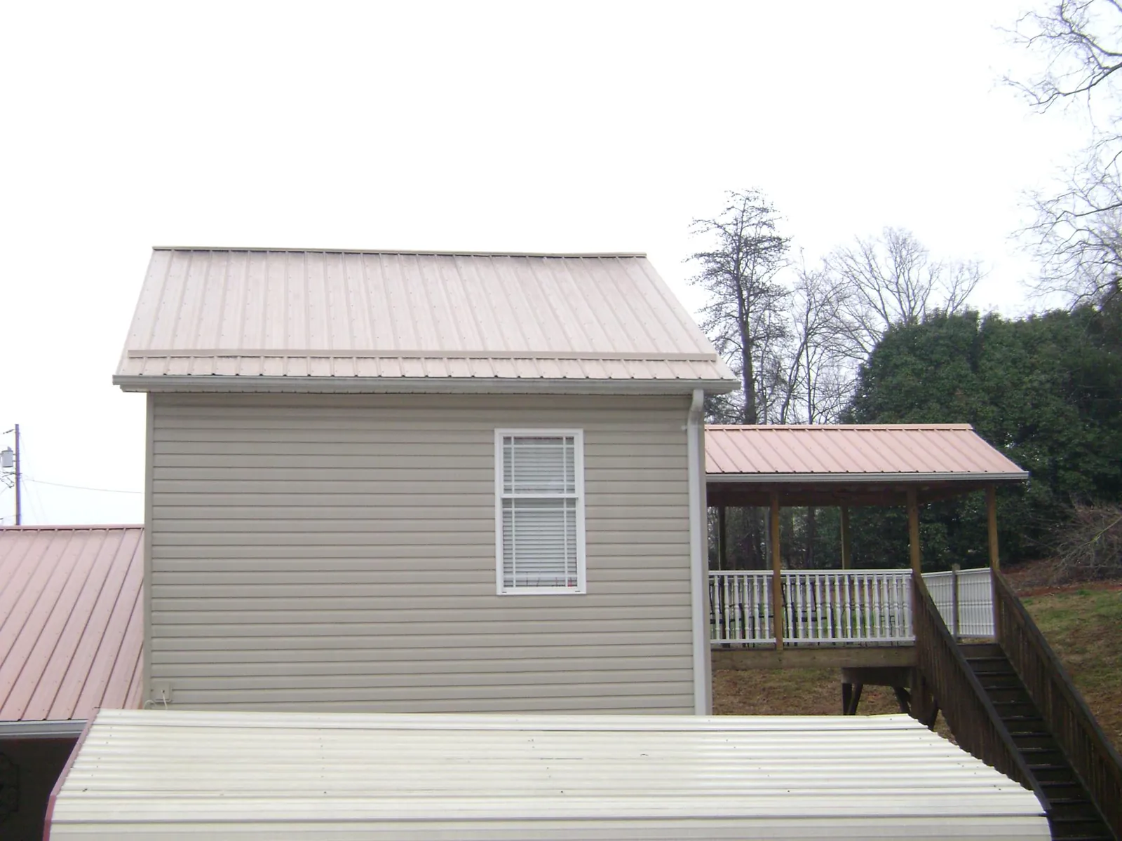 Tan metal roofs on a two story addition and attached porch, from a Roof Replacement job in Du Bois